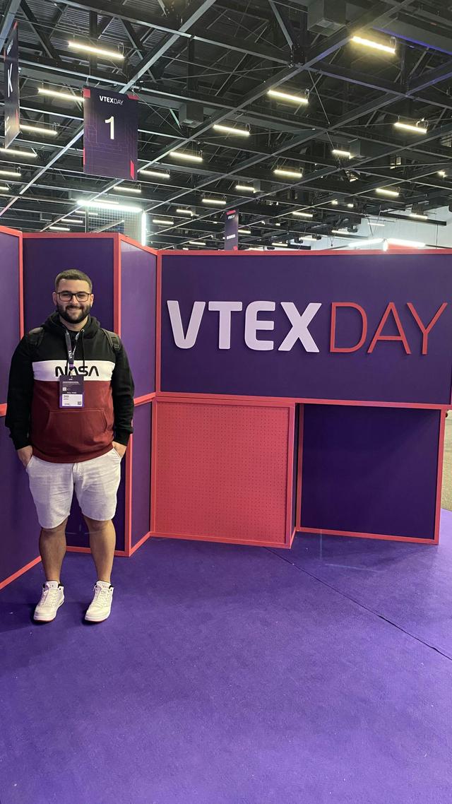 Foto do Denner com o painel do evento VTEX Day