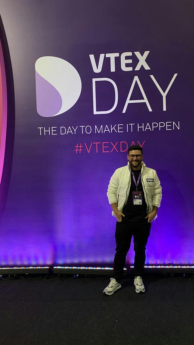 Foto de Denner Azevedo com o painel do VTEX Day 2023 ao fundo